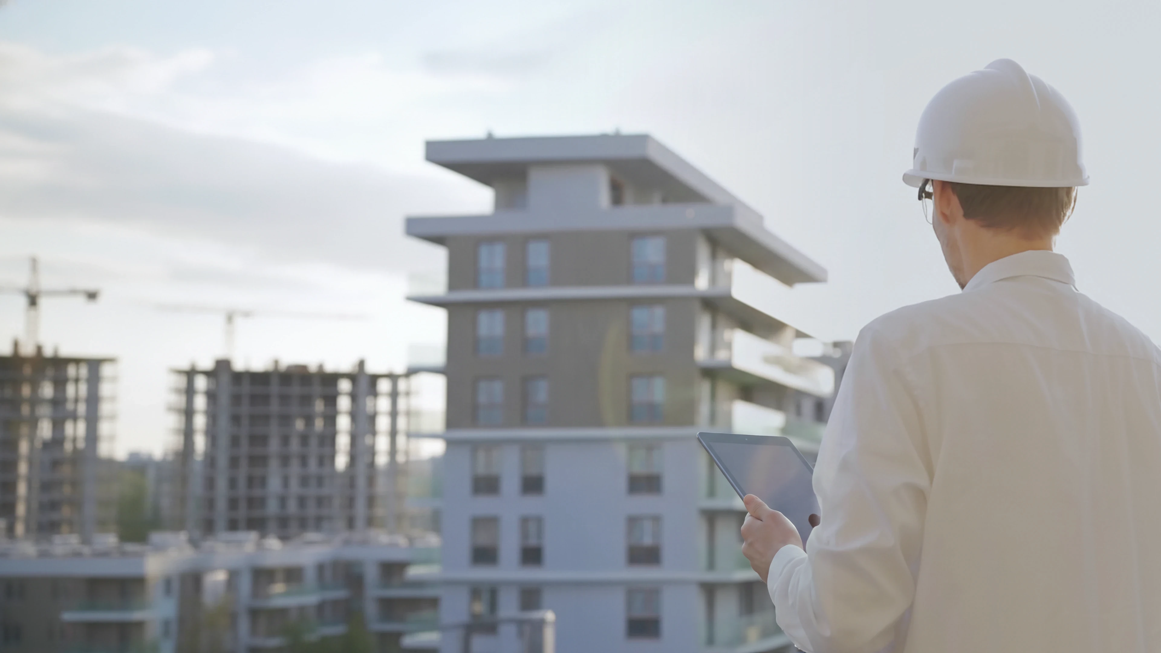 Site engineer in a hard hat reviewing a checklist in front of a residential building under construction